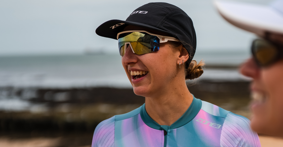 Person wearing a zone3 5 panel running black cap and colorful sunglasses with a blurred background