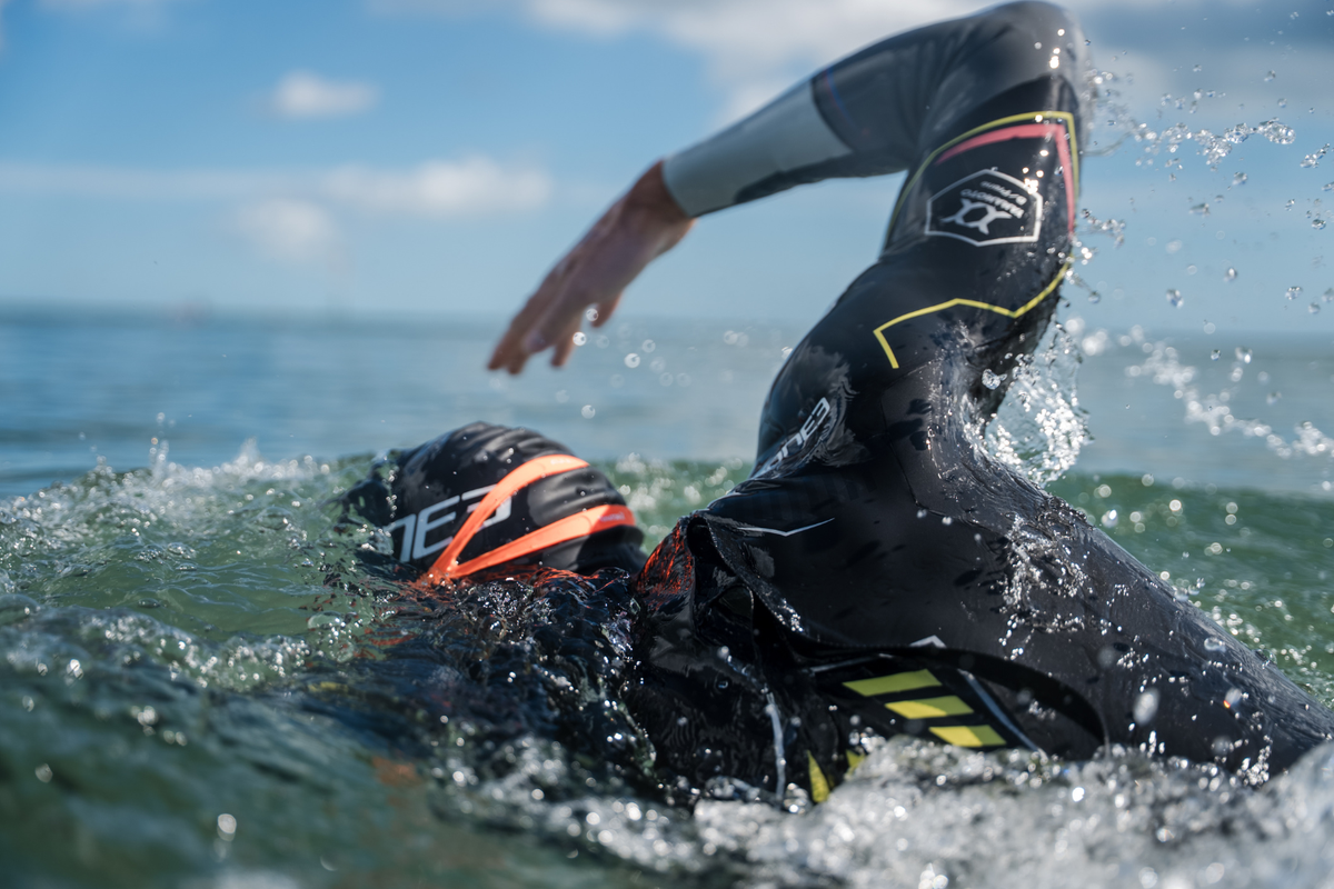 Person swimming in the sea. Wearing a ZONE3 wetsuit, black swim cap and orange goggles