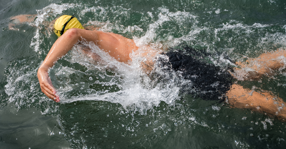 Person swimming in a pool wearing zone3 black jammers and  a yellow swim cap.