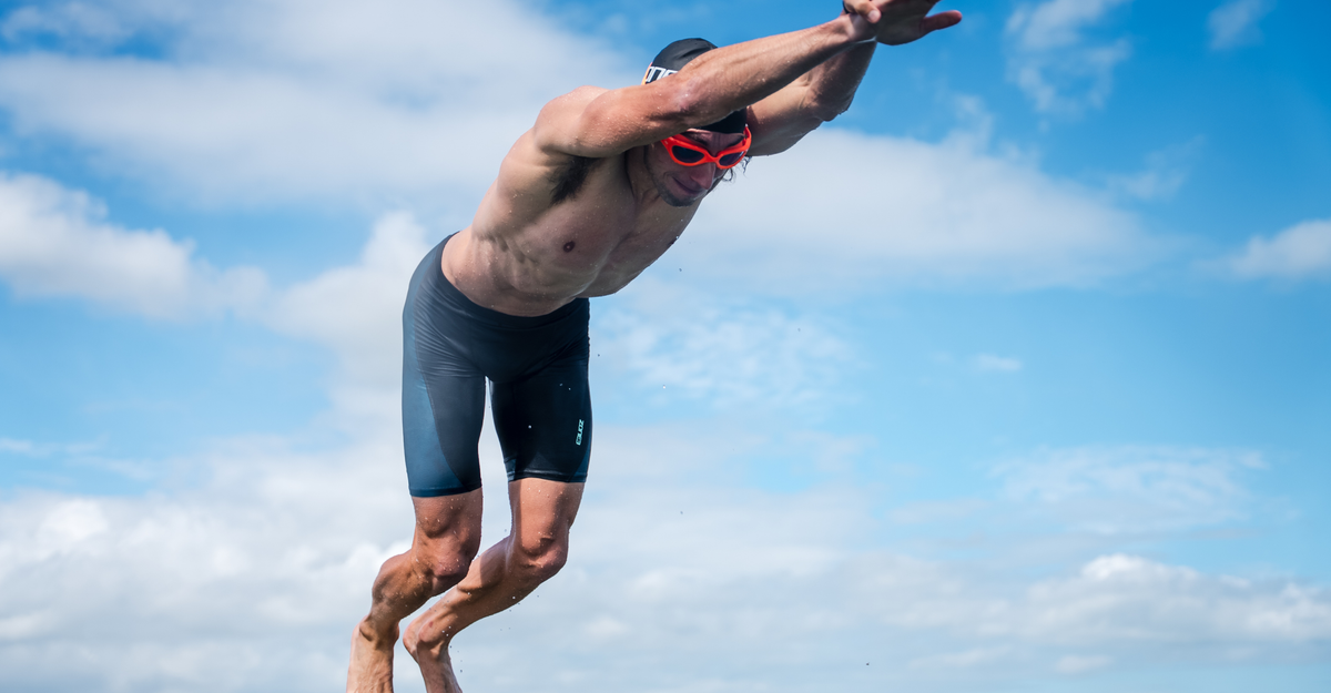 Person wearing the black and teal jammers diving into water with a clear blue sky in the background