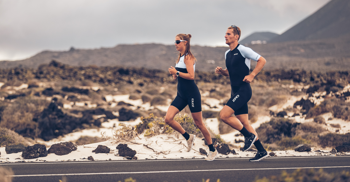Two runners in lava trisuit running on a road with a mountainous landscape in the background.