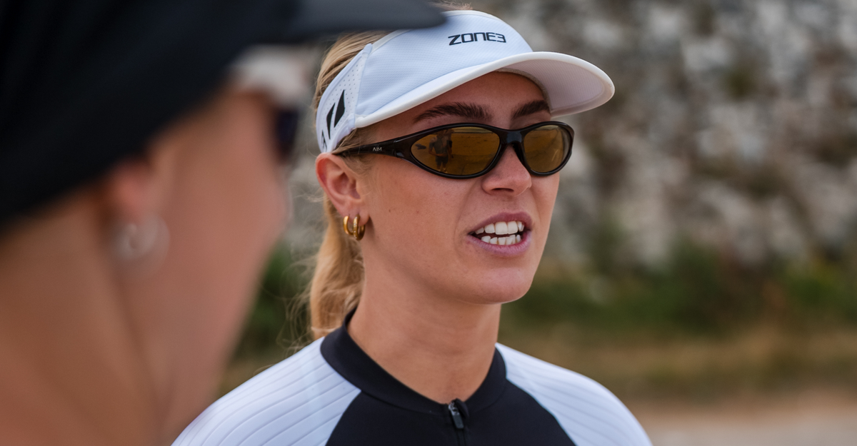 Woman wearing glasses and a zone3 white running visor with a zone3 logo on a blurred background